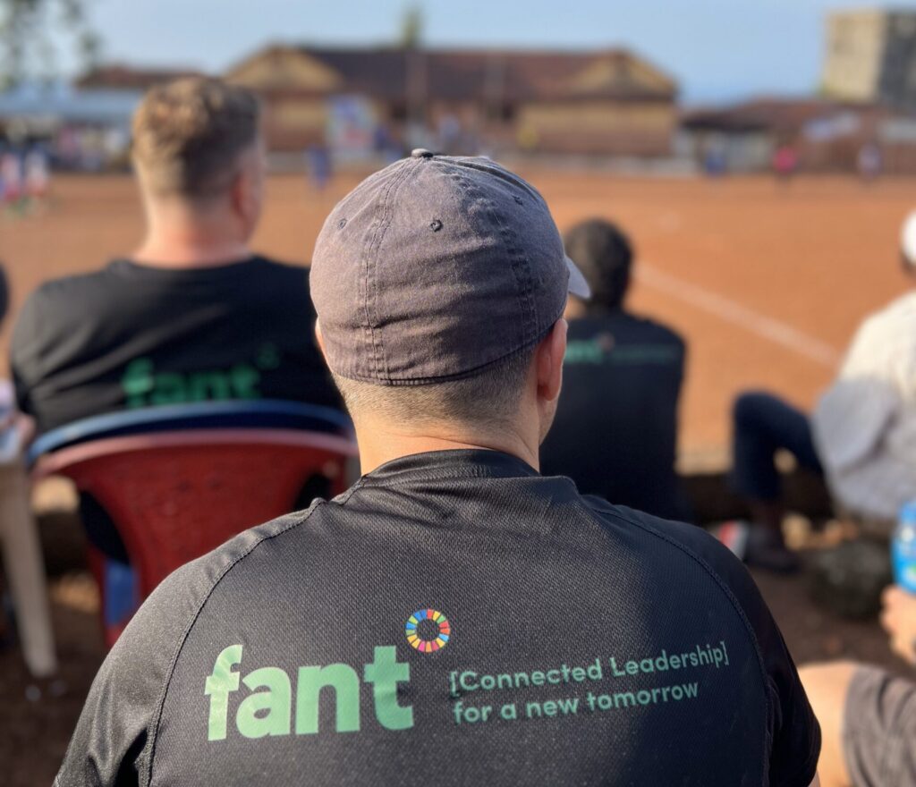 En deltager på Connected Leadership-kurset i Sierra Leone er fotograferet bagpå, mens de ser på en lokal fodboldkamp. Bagpå deres tshirt er FANTs logo.