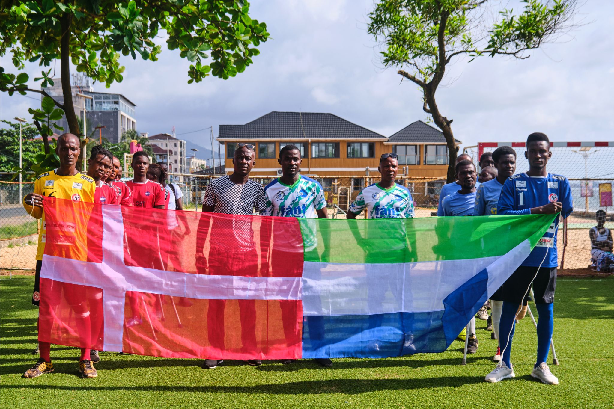 Gruppe holder det danske flag og det sierra leonske flag på en kunstgræsbane i Sierra Leone